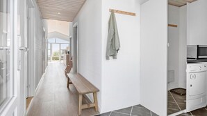 Eine moderne Küche mit Einbauofen und Mikrowelle, eine Holzbänkschwelle in einem Flur und ein Blick ins Freie durch große Fenster.