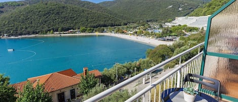 A balcony with a table and chair overlooking a coastal area with a beach and hills.