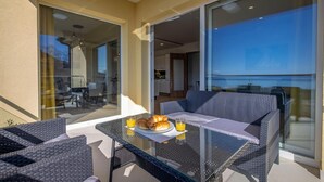 Un balcone con mobili in vimini, un tavolo in vetro e articoli per la colazione.