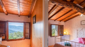 A cozy bedroom with wooden walls, a large window offering a mountain view, a bed with pink bedding, and a nightstand with a lamp. - Beautiful apartment for 5 guests with WIFI, private pool, TV and pets allowed (Lugnano-monti Di Villa)
