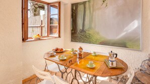 A dining area with a wooden table set for four, surrounded by white chairs. A large painting of a forest scene is on the wall. - Beautiful apartment for 5 guests with WIFI, private pool, TV and pets allowed (Lugnano-monti Di Villa)