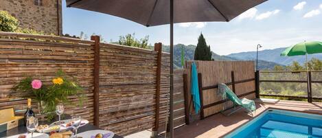 Relax by the pool surrounded by a mountainous landscape, with a shaded dining area and a small slide for kids.