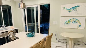 A modern kitchen with a large island, wicker chairs, a round table, and artwork of shrimp on the wall. - Unwind at our beautifull dog friendly beach with private access! (Vero Beach)