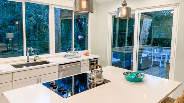 A modern kitchen with a central island, stainless steel appliances, and large windows offering a view of an outdoor deck. - Unwind at our beautifull dog friendly beach with private access! (Vero Beach)