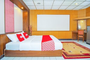 Ein Hotelzimmer mit einem hölzernen Bett, einer großen Whiteboard-Tafel, einem Schreibtisch mit Stuhl und einem Teppich mit rotem und weißem Muster.