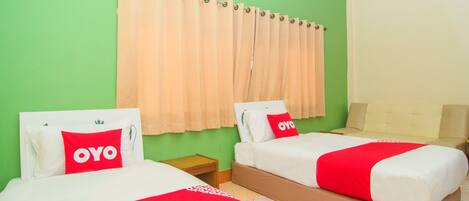 A hotel room with two beds, each with a red and white bedspread and pillows, a green wall, and a beige sofa.