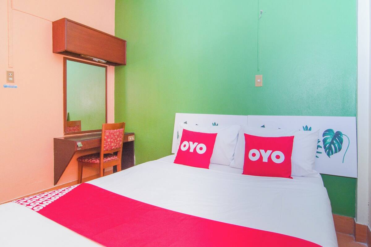 Une chambre d’hôtel avec un lit, un bureau et une chaise. Le lit est agrémenté de deux oreillers sur lesquels est inscrit le mot « OYO ».