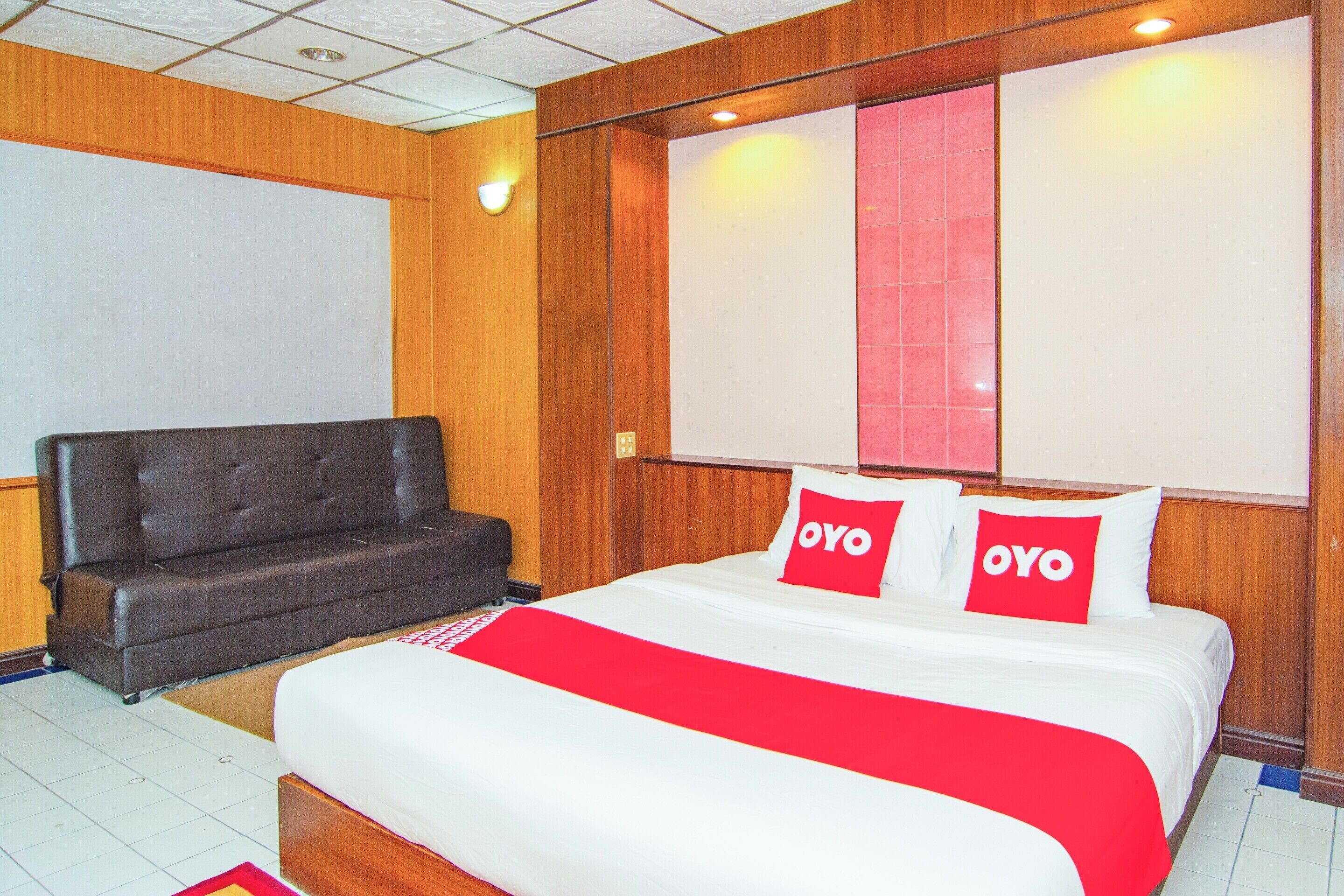 A hotel room with a large bed, a sofa, and a wooden wall panel.