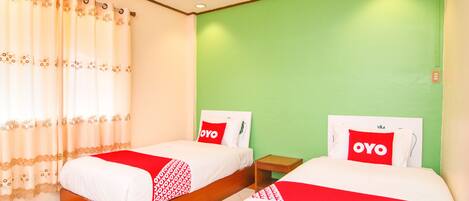 Dos camas individuales con ropa de cama roja y blanca, una pared verde y un techo de madera.