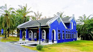 A blue building with arched windows and a tiled roof, surrounded by palm trees. - OYO Bulan Anda Baba Resort (Ao Luek)