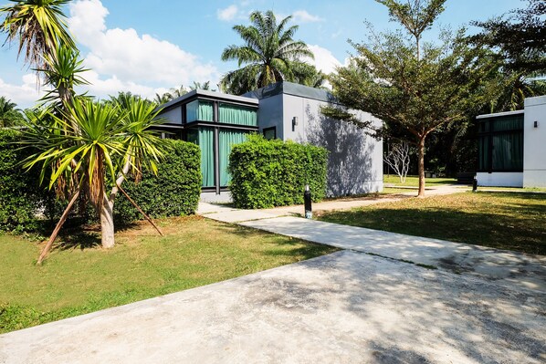 A modern building with a concrete pathway, surrounded by lush greenery and palm trees.