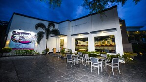 An outdoor dining area with tables and chairs, a palm tree, and a building with a sign. - Maria Eloisa Royal House (Daanbantayan)