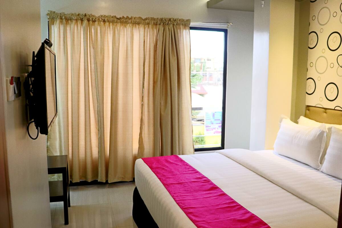 Une chambre d’hôtel avec un lit, des rideaux, une fenêtre et un mur orné d’un motif circulaire.