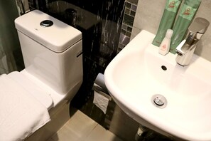 Une salle de bain avec des toilettes blanches, un lavabo et un miroir.