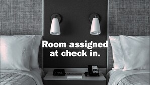 Une chambre d’hôtel avec deux lits, une table de chevet avec une horloge et un téléphone, et deux lampes fixées au mur.