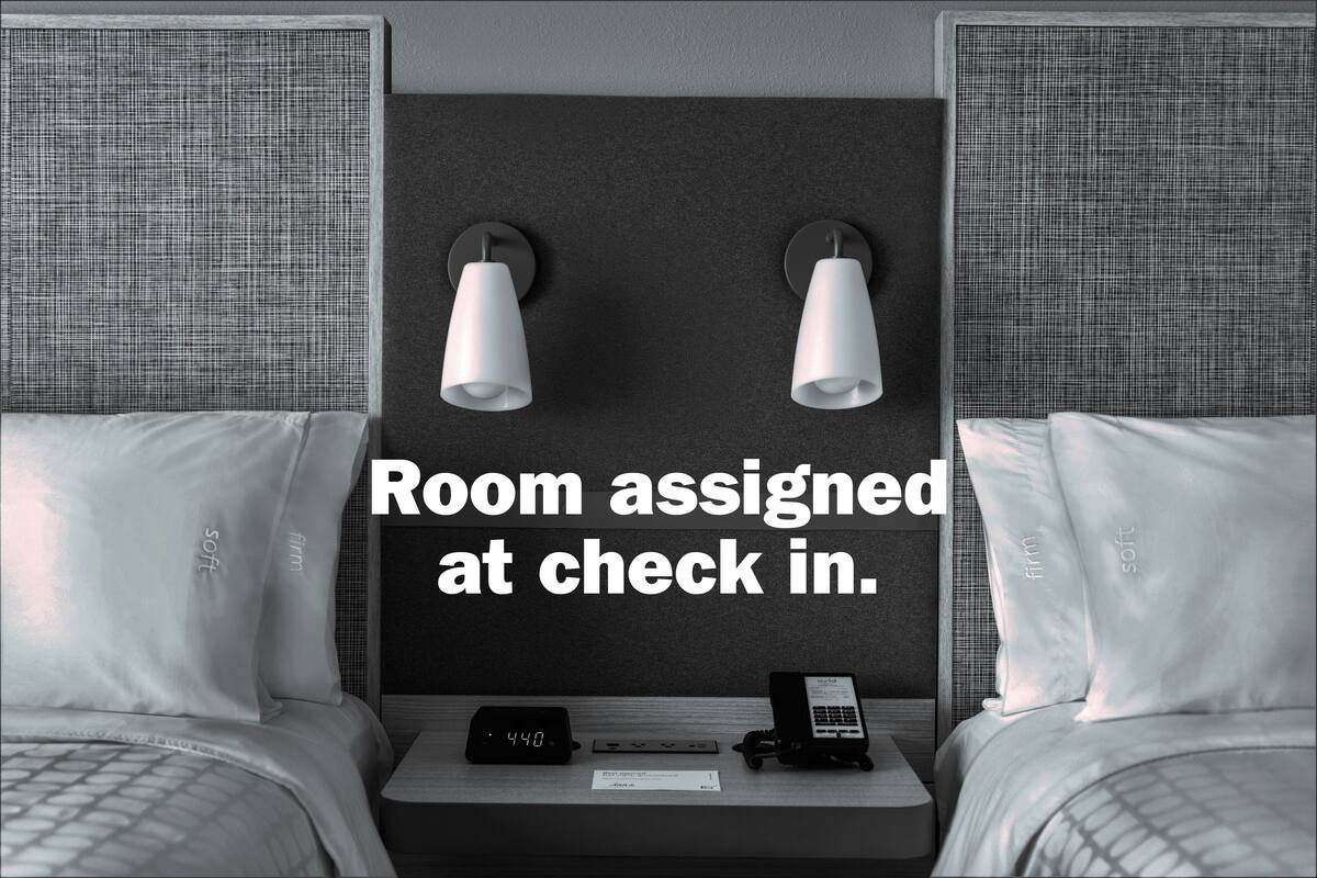 A hotel room with two beds, a nightstand with a clock and phone, and two wall-mounted lamps.