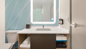 Une salle de bain avec un lavabo blanc, un miroir, un porte-serviettes et des toilettes.