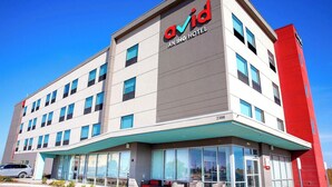 Un bâtiment d’hôtel moderne, avec une enseigne « Ovid » bien visible, de nombreuses fenêtres et un mur d’accent rouge.