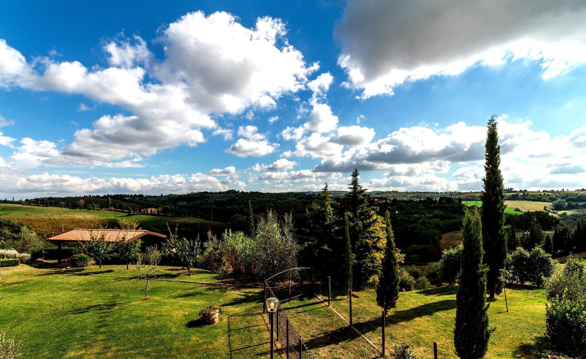 A rural landscape with a clear sky, rolling hills, and a fenced garden area.