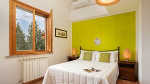 Une chambre à coucher avec un lit, deux tables de chevet, une fenêtre, un radiateur et un mur d’accent de couleur verte.