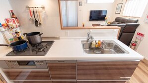 A compact kitchen with a stove, sink, and wooden cabinetry. - Mori House In Nishinippori (Tokyo)