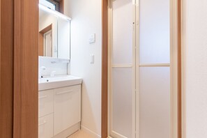 A bathroom with a white sink, mirror, and frosted glass shower door. - Mori House In Nishinippori (Tokyo)