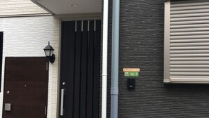 A building with a black gate, a white tiled entrance, a mailbox, and a sign indicating a business hours of 12-7. - Mori House In Nishinippori (Tokyo)