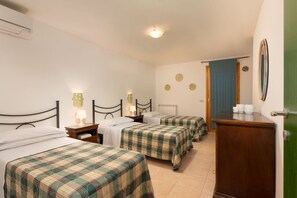 Une chambre avec trois lits, une commode en bois et une porte dotée d’un miroir.