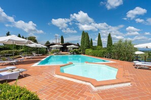 Une piscine rectangulaire, bordée d’une terrasse carrelée, entourée de chaises longues et de parasols.