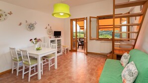 A cozy room with a dining table, chairs, a green sofa, a TV, and a view of the countryside through a window. - Cosy apartment with WIFI, A/C, pool, TV, terrace and panoramic view, close to San Gimignano (Sughera)