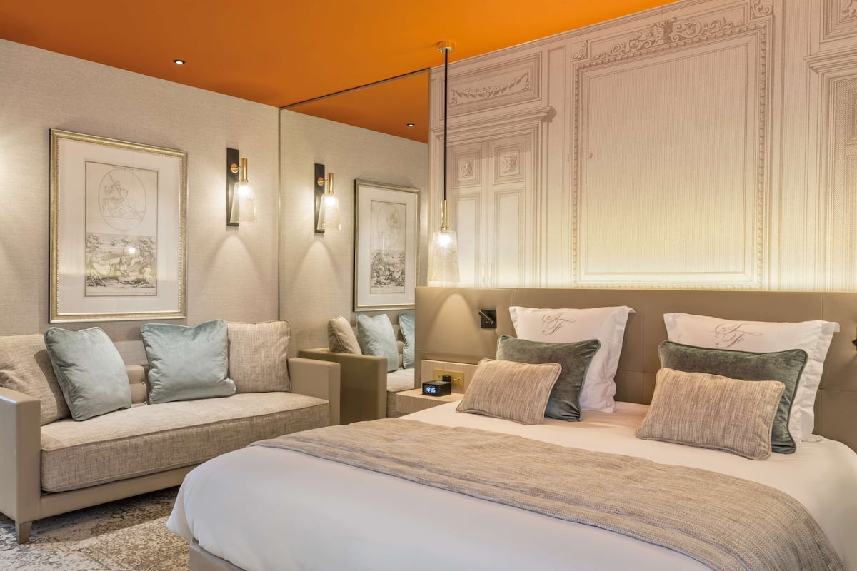 A modern bedroom with a large bed, a sofa, and two wall-mounted reading lights.
