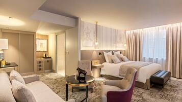 Quarto de hotel com uma cama, duas poltronas, uma mesinha, mesa de cabeceira, abajur, espelho e guarda-roupa.