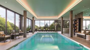 Una piscina interior moderna con amplios ventanales, mobiliario de mimbre y vistas al paisaje circundante.