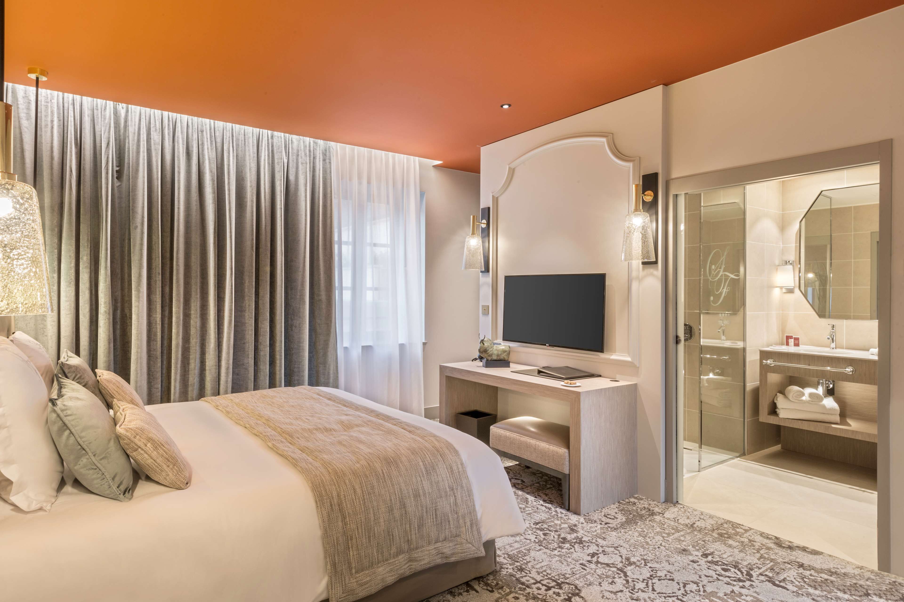 Een hotelkamer met een bed, een bureau, een televisie, een badkamer met spiegel en douche.