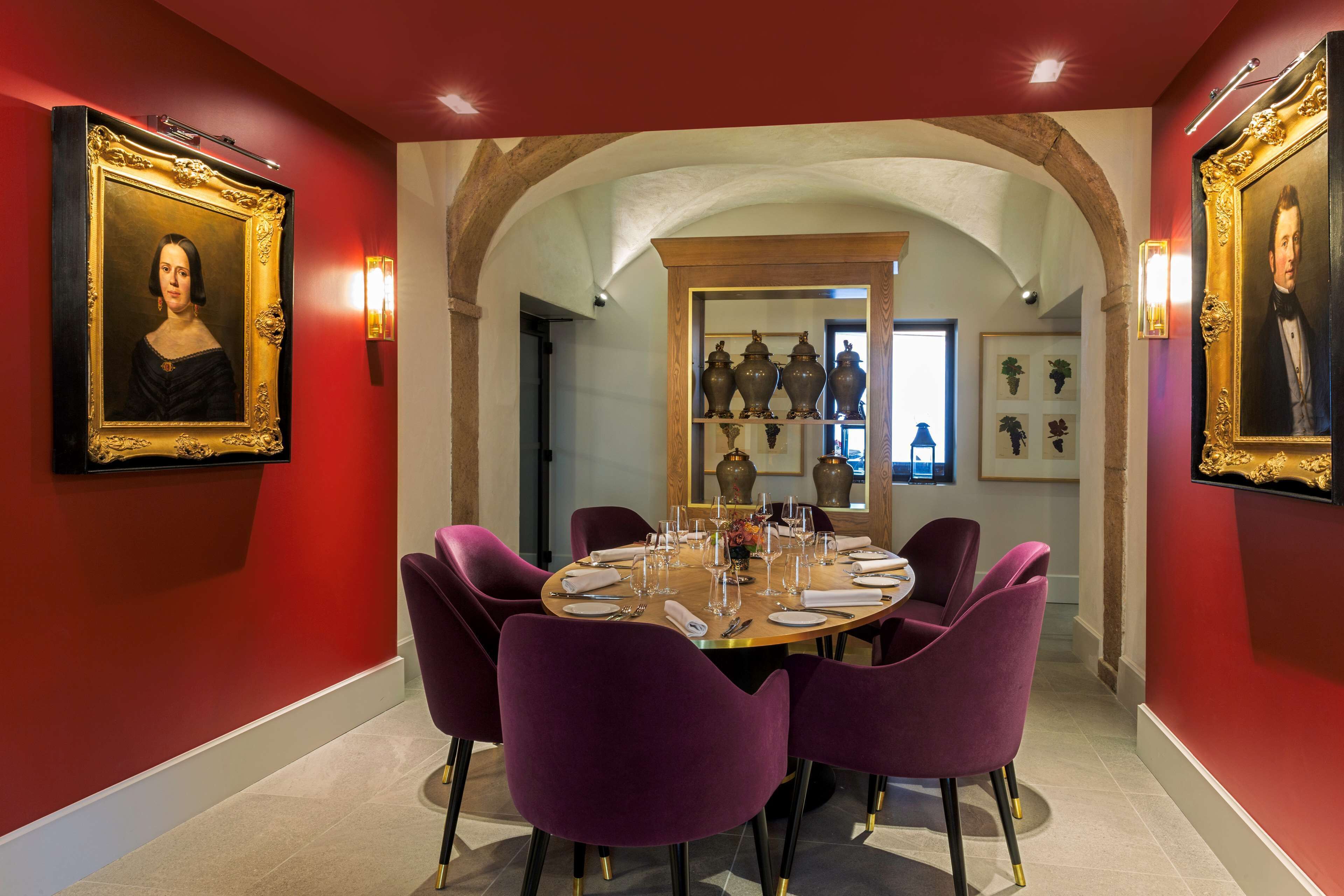 A dining room with a round table, purple chairs, and framed portraits on the walls.