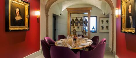 A dining room with a round table, purple chairs, and framed portraits on the walls.
