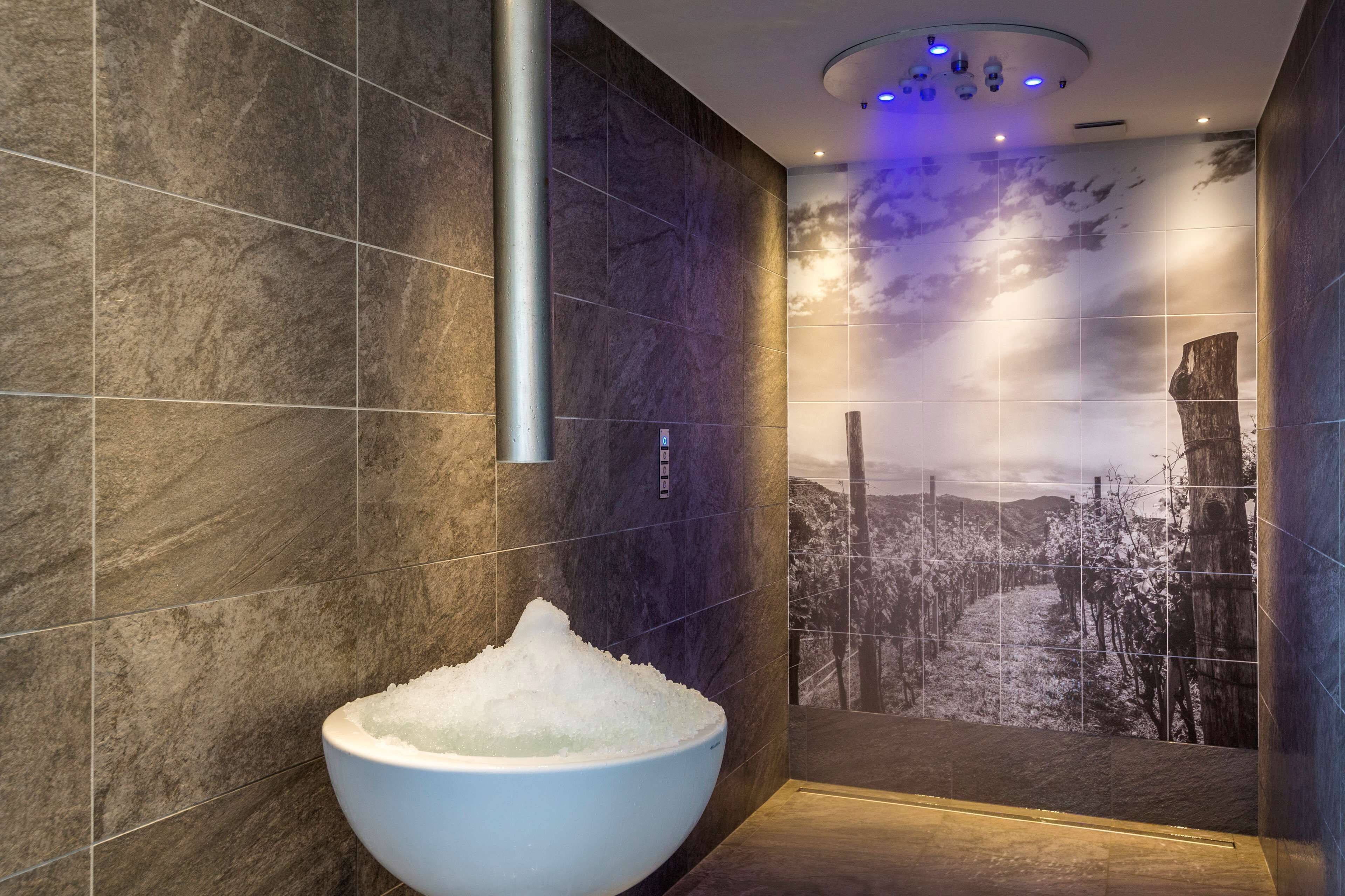 Un bagno moderno con un lavabo bianco e ampio pieno d'acqua, pareti piastrellate scure e un affresco raffigurante un paesaggio innevato.