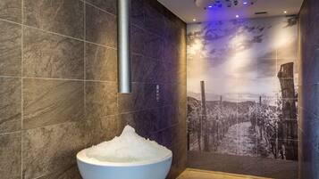 A modern bathroom with a large white basin filled with water, dark tiled walls, and a mural of a snowy landscape.
