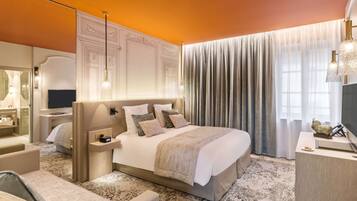 A hotel room with a large bed, a desk with a television, a bedside table, and a bathroom visible through an open door.