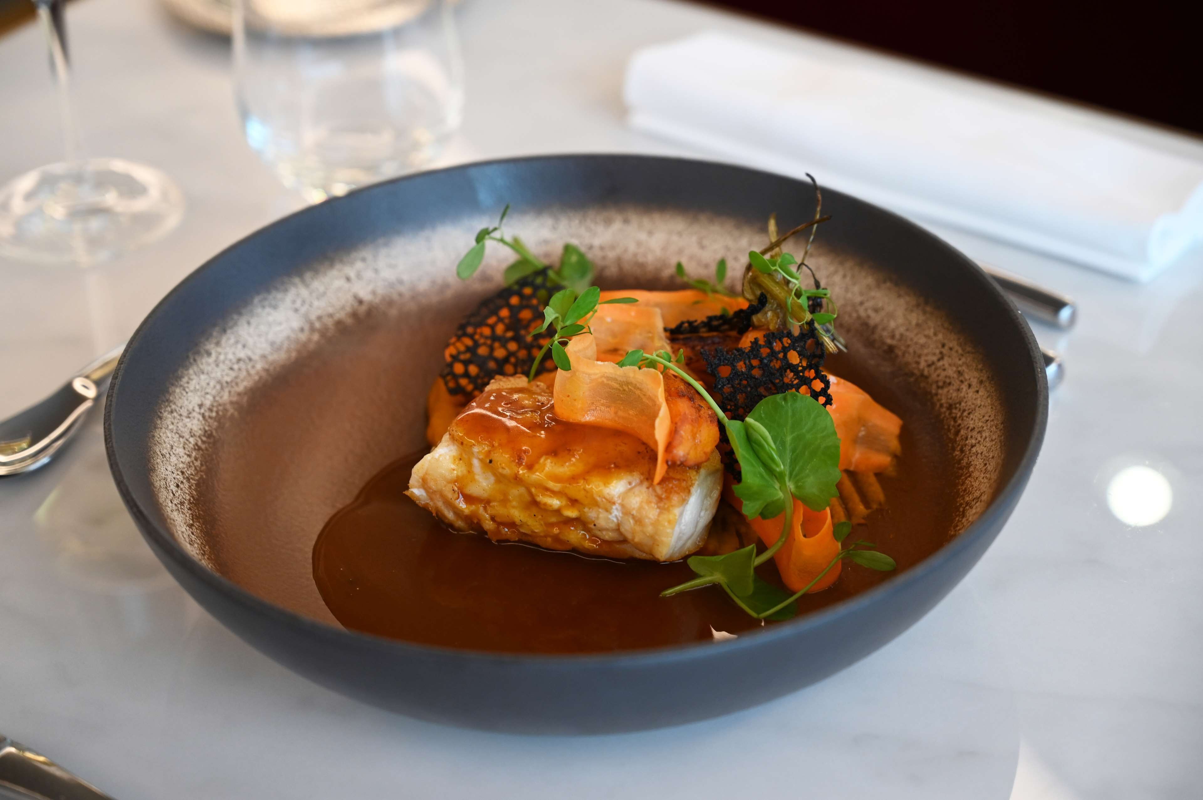 Ein Gericht mit Fisch, Garnitur und Soße in einer Schüssel.
