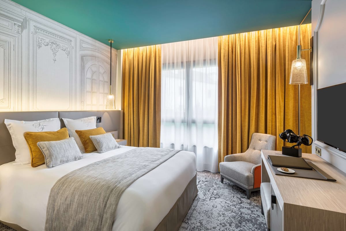 A modern hotel room with a large bed, a desk, and a chair.