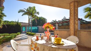 An outdoor patio with a table set for two, featuring a tablecloth with a fruit pattern, a vase with flowers, and a yellow cup. - Beautiful home in Santa Croce Camerina with WiFi (Santa Croce Camerina)