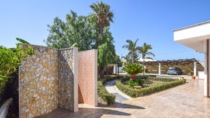 A modern house with a stone wall, a paved driveway, and a car parked under a pergola. - Beautiful home in Santa Croce Camerina with WiFi (Santa Croce Camerina)