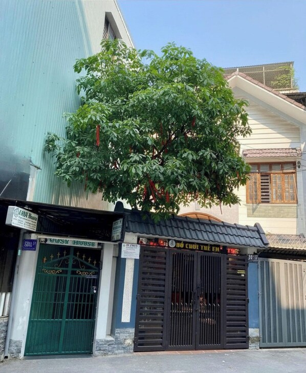 A building with a large tree in front, a sign for a house, and a closed gate. - Cosy House Da Nang (Da Nang)
