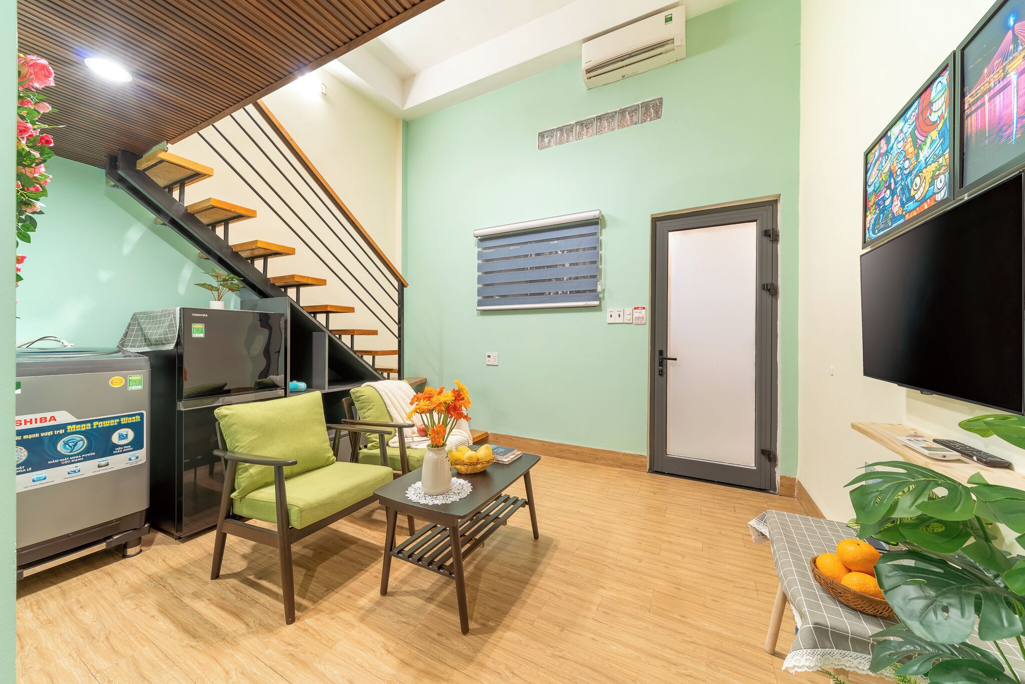 A living room with a sofa, a coffee table, a TV, a staircase, and a refrigerator.