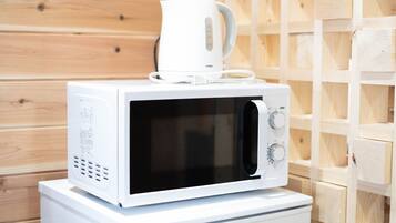 A white microwave on a white appliance, with a white kettle on top, against a wooden wall background.