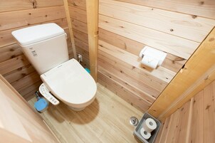 Un baño pequeño con paneles de madera, un inodoro, un bidé y un dispensador de papel higiénico.