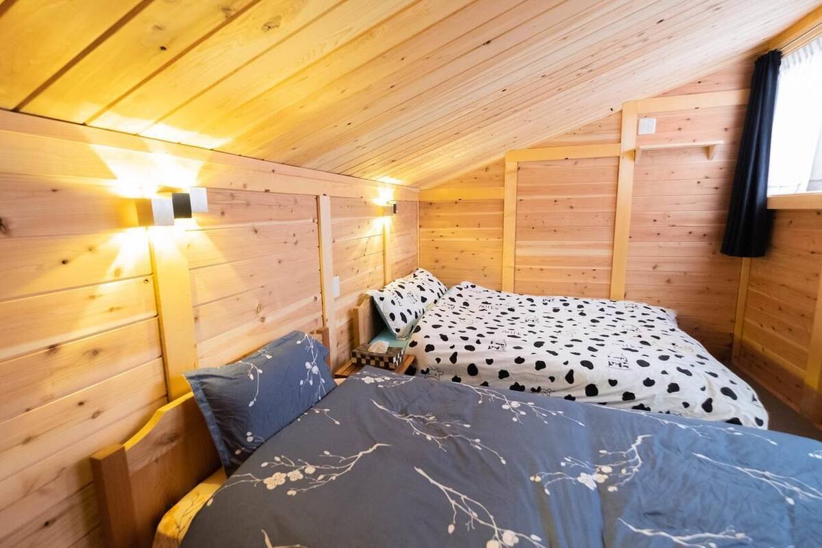 A cozy wooden cabin room with a bed, a nightstand, and a wall-mounted light fixture.