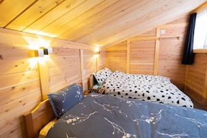 Una habitación acogedora tipo cabaña de madera, con una cama, una mesita de noche y una lámpara fijada a la pared.