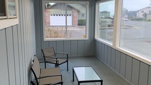 Ein überdachter Außenbereich mit vier Stühlen und einem kleinen Tisch, große Fenster mit Blick auf eine Wohnstraße.